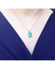 Person wearing a necklace with an emerald pendant against a dark blue background