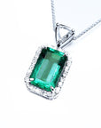 A rectangular emerald encircled by a halo diamond pendant with a top bail with trillion-cut diamond in white gold.