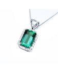 A rectangular emerald encircled by a halo diamond pendant with a top bail with trillion-cut diamond in white gold.