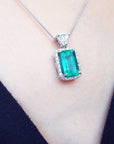 Emerald green gemstone pendant on a white gold chain against a dark background.