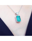 Emerald green gemstone pendant on a white gold chain against a dark background.