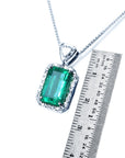 Emerald pendant on a chain with a ruler for scale on a white background