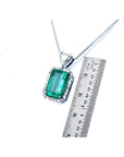Emerald pendant on a chain with a ruler for scale on a white background