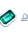 Green emerald and clear diamond on a white background showing the handcrafted setting on the rough.