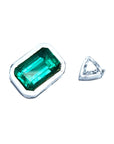 GIA certified medium-deep green Colombian emerald, emerald-cut, set in a white gold bezel next to a small triangular diamond.