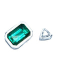 GIA certified medium-deep green Colombian emerald, emerald-cut, set in a white gold bezel next to a small triangular diamond.