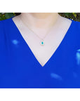 0.75 ct GIA F1 Colombian emerald pendant with diamond halo on 18k yellow gold chain, worn on a blue top.