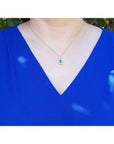 0.75 ct GIA F1 Colombian emerald pendant with diamond halo on 18k yellow gold chain, worn on a blue top.