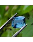 6.07 ct GIA certified rectangular emerald-cut natural untreated blue-green sapphire held by tweezers.