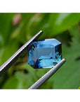 6.07 ct GIA certified rectangular emerald-cut natural untreated blue-green sapphire held by tweezers.