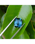 6.07 ct GIA certified natural untreated rectangular emerald-cut blue-green sapphire on a green leaf.