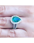 Brides' emerald engagement ring with a halo diamond crafted in white gold on a finger.