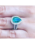 Brides' emerald engagement ring with a halo diamond crafted in white gold on a finger.