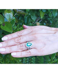 18K white gold ring with a 4.02 ct pear-shaped emerald surrounded by natural diamonds on a woman's hand.