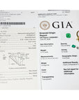GIA diamond grading report and emerald origin report with a gold ring featuring a green gemstone on a white background.