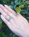 A hand wearing a cushion cut natural colombian emerald ring on a leafy background.