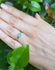 Hand wearing a minimalist emerald solitaire ring representing May's birthstone jewelry with a green leafy background.