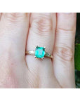 A 14k yellow gold natural Muzo colombian emerald ring with side diamonds on a person's finger.