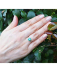 14K yellow gold emerald ring with baguette side diamonds on a hand, against green leaves.