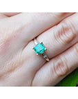 14K yellow gold ring with a vibrant emerald and baguette side diamonds on a finger.