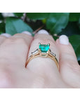 14K yellow gold ring with a vibrant emerald center stone and baguette side diamonds on a hand.