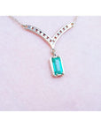 14K yellow gold necklace with a baguette-cut Colombian emerald pendant and diamond-studded V-shaped centerpiece.
