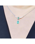 Pear shaped emerald and diamond necklace in 14K white gold on a black top.