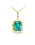 A natural emerald-cut colombian emerald surrounded by a halo diamond pendant in yellow gold.