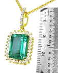 Gold pendant with a natural emerald next to a ruler for scale on a white background.