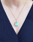 Gold necklace with a natural colombian emerald pendant on a woman wearing a dark blue top.
