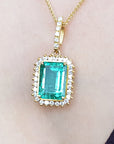 Gold pendant with a square natural emerald on a woman wearing a black top.