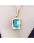 Emerald-cut emerald pendant with halo diamonds in 18K gold, worn on a necklace.