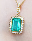 A yellow gold emerald-cut natural emerald pendant with a halo diamond on a person's neck.