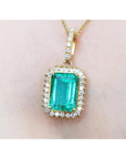 A yellow gold emerald-cut natural emerald pendant with a halo diamond on a person's neck.