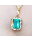 A 18k yellow gold emerald-cut natural emerald pendant with a halo diamond on a person's neck.