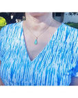 Ethiopian opal pear pendant necklace with blue-violet play-of-color in 14K yellow gold on a woman.