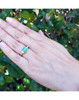 1.51 ct. emerald and trillion cut diamonds ring in 18k gold on a hand.