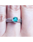 A white gold emerald ring with diamonds accents on a person's finger.