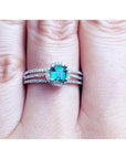 A white gold emerald ring with diamonds accents on a person's finger.
