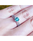 Emerald engagement ring with halo diamonds on a 14K white gold triple-row band, worn on a finger.