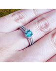 Emerald engagement ring with halo diamonds on a 14K white gold triple-row band, worn on a finger.