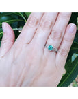 Emerald engagement ring with halo diamonds on a 14K white gold band, worn on a hand.