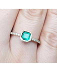 A 14k yellow gold colombian emerald ring bezel set with accent diamonds on a finger.