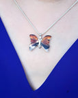 Sterling silver agate butterfly pendant necklace with orange, brown, and black hues on a blue top.