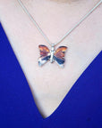 Sterling silver agate butterfly pendant necklace with orange, brown, and black hues on a blue top.