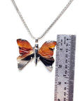Butterfly-shaped pendant on a chain with a ruler for scale on a white background