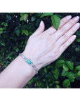 14K white gold paper clip bracelet with a rectangular emerald and diamond halo on a woman's wrist.