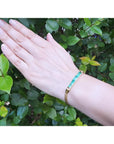 14K gold bracelet with five vibrant bluish-green emeralds and diamonds on a woman's wrist.