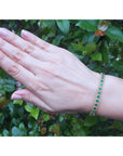 A woman's hand wearing a emerald bangle bracelet with a leafy background.