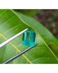 2.95 carat emerald-cut loose Colombian emerald with vibrant medium green color, held by tweezers.